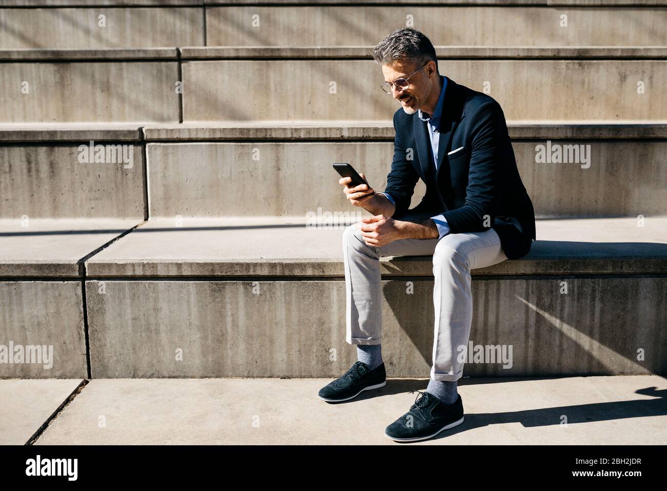 Gray-haired businessman sitting on stairs using cell phone Stock Photo