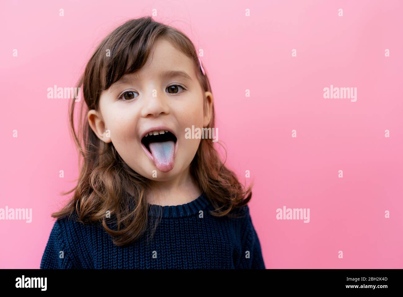 Portrait of little girl sticking out blue tongue in front of pink background Stock Photo