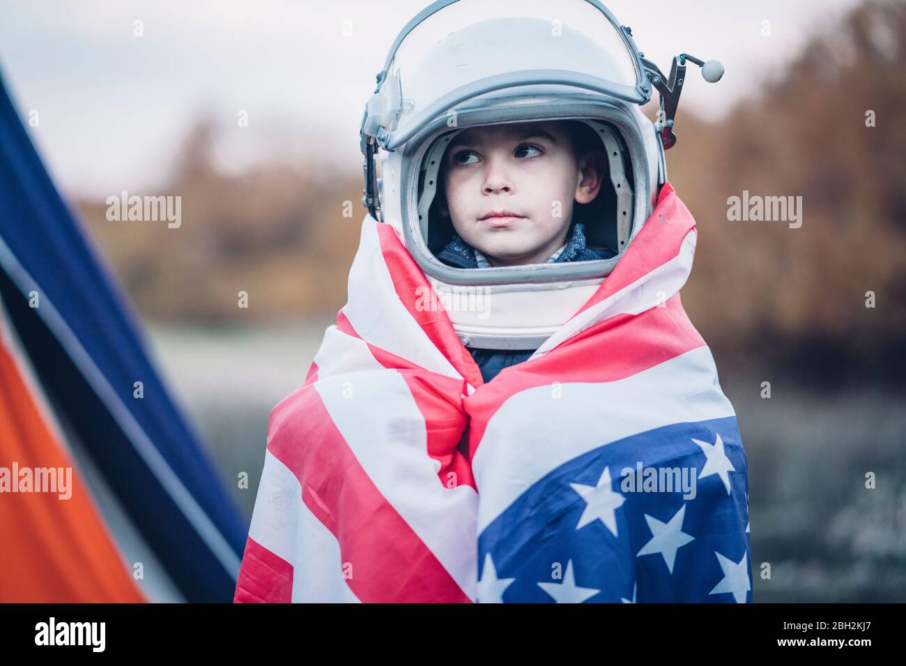 Portrait of little boy wrapped in American flag wearing space helmet Stock Photo
