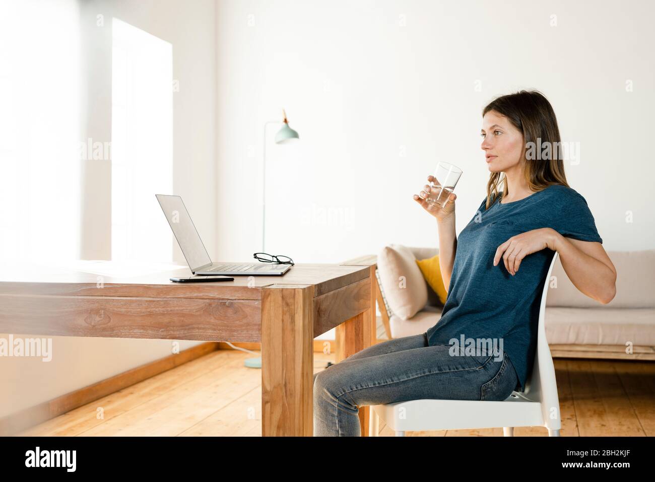 Young woman drinking a galss of water and having a break from working at laptop in home office Stock Photo