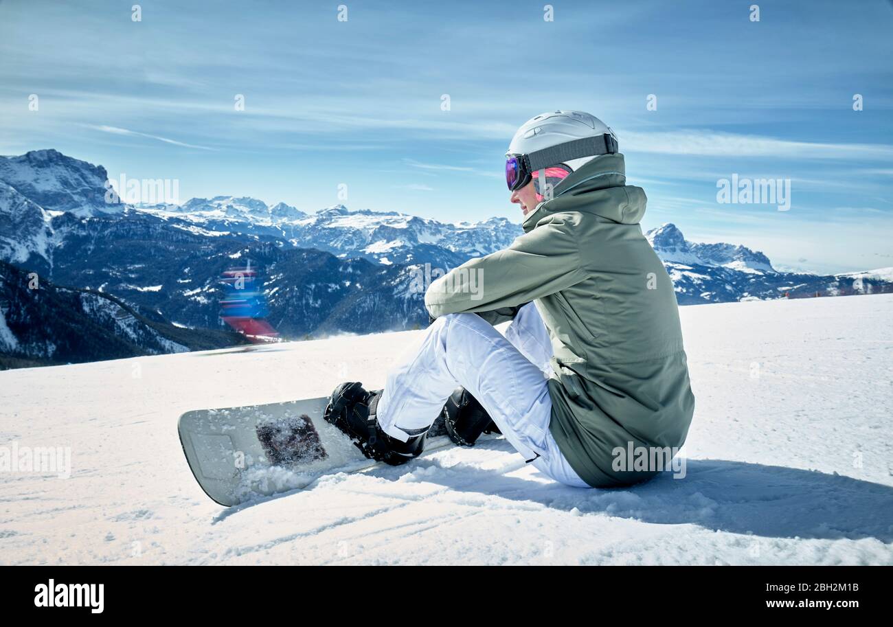 Smiling woman sitting with snowboard on viewpoint and enjoying view at distance Stock Photo