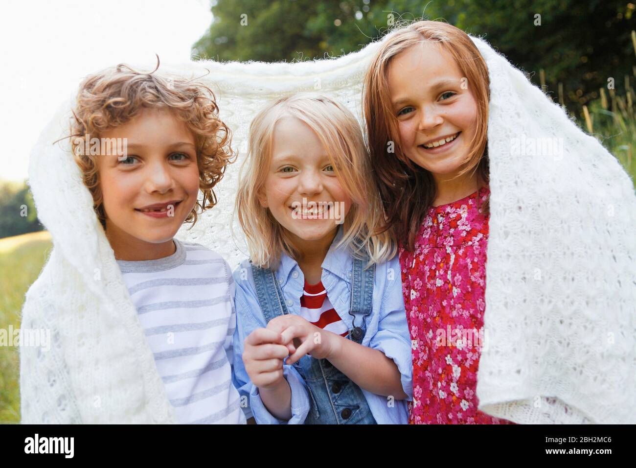 Portrait of happy children wrapped in blanket outdoors Stock Photo