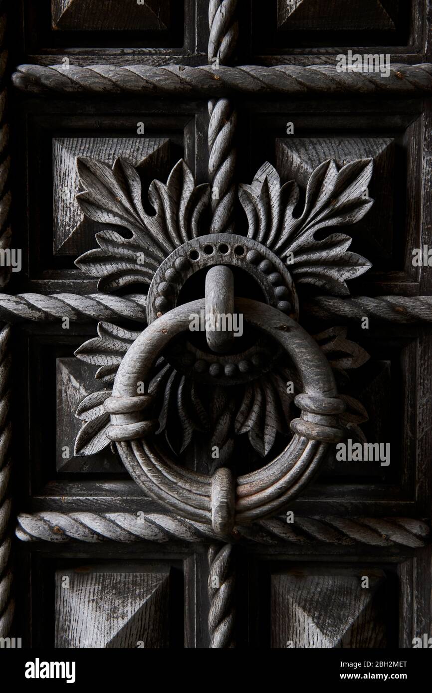 Detailed close-up of large ancient hand carved wooden door and round knocker Stock Photo