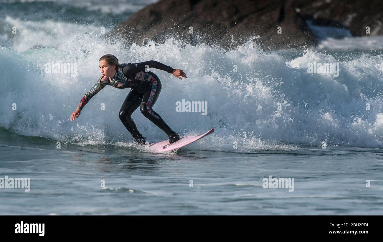 A panoramic image of a young female surfer riding a wave at Fistral in Newquay in Cornwall. Stock Photo