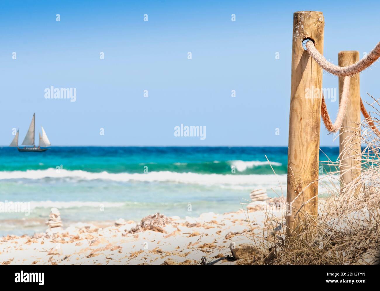 Rustic fence with wooden poles and rope on a deserted beach, in the background the rough sea. A wild beach in the island of Formentera Spain Stock Photo