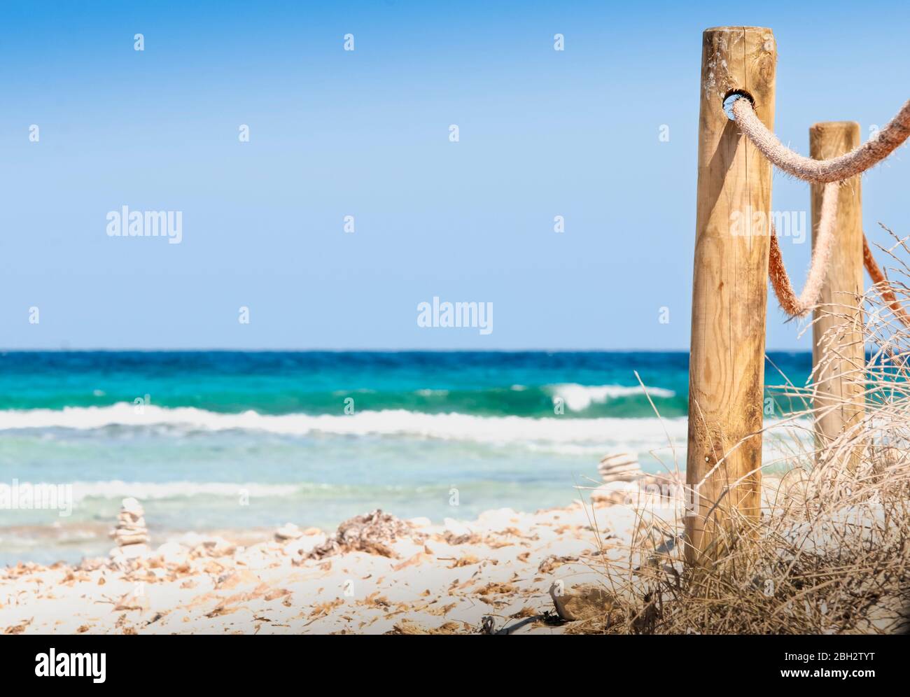 Rustic fence with wooden poles and rope on a deserted beach, in the background the rough sea. A Wild beach on the island of Formentera Spain. Stock Photo
