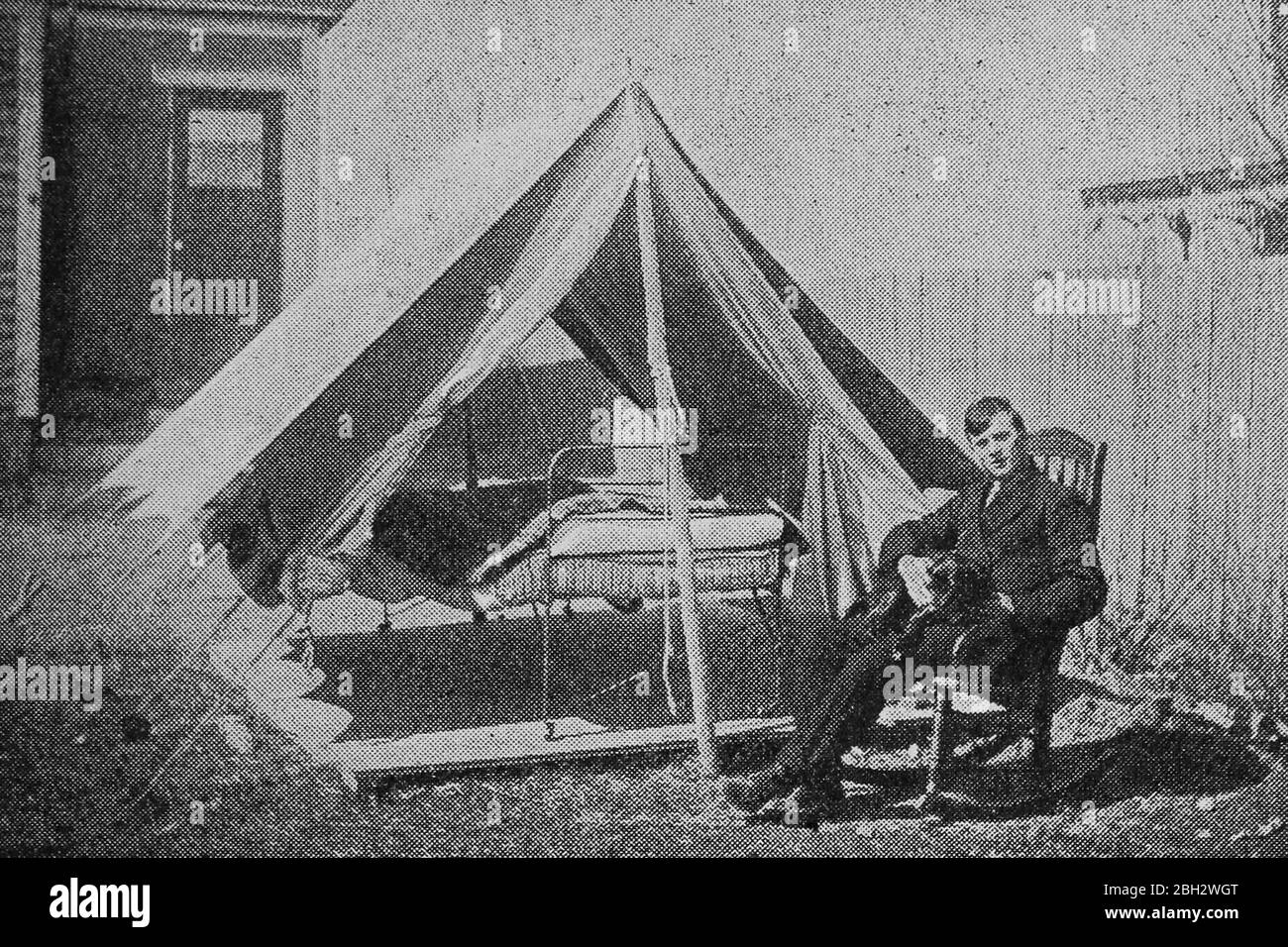 Image from the book 'Epidemics, How to Meet Them' by Louis A. Hansen, featuring a man sitting in front of a tent with a hospital bed in it, likely a quarantine or isolation tent, published by Review and Herald Publishing Association, 1919. Courtesy Internet Archive. () Stock Photo