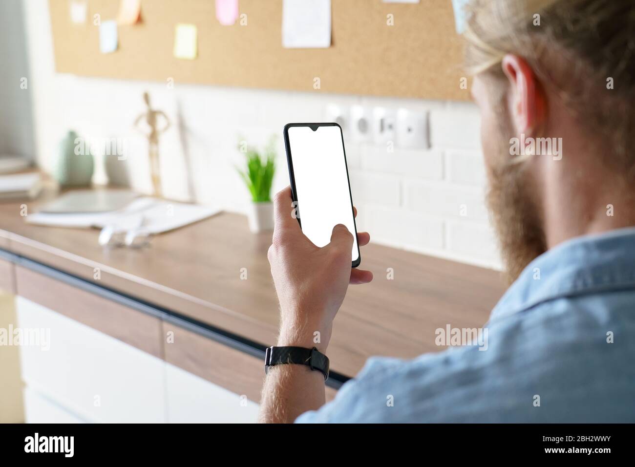 Man using smart phone mock up white screen, over shoulder view. Stock Photo