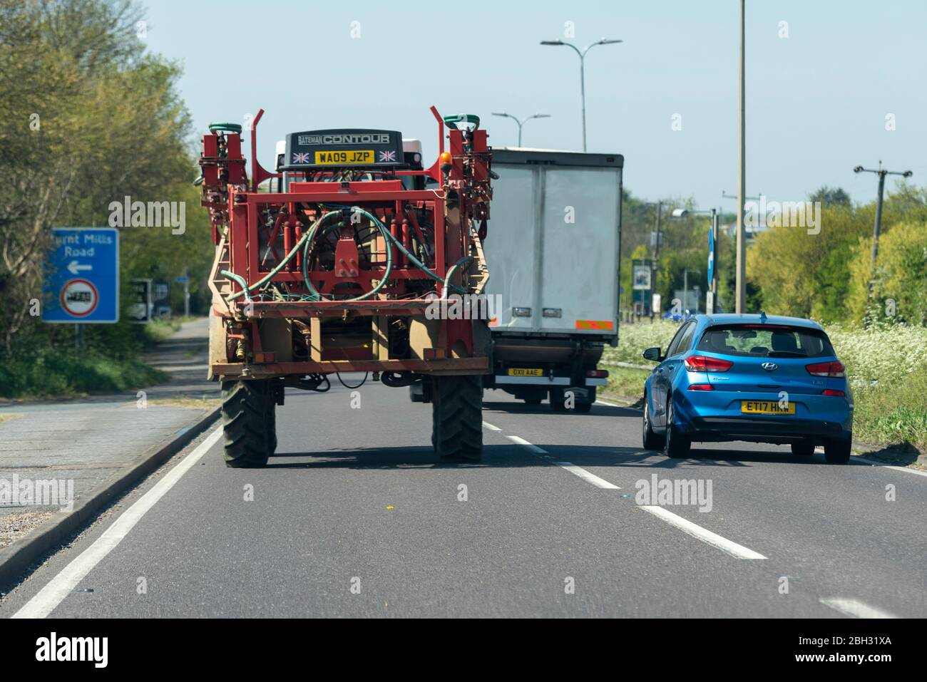 Farm vehicle driving in traffic on A127 arterial, road Essex. Slow agricultural tractor being overtaken by lorry, truck, holding up vehicles. Industry Stock Photo