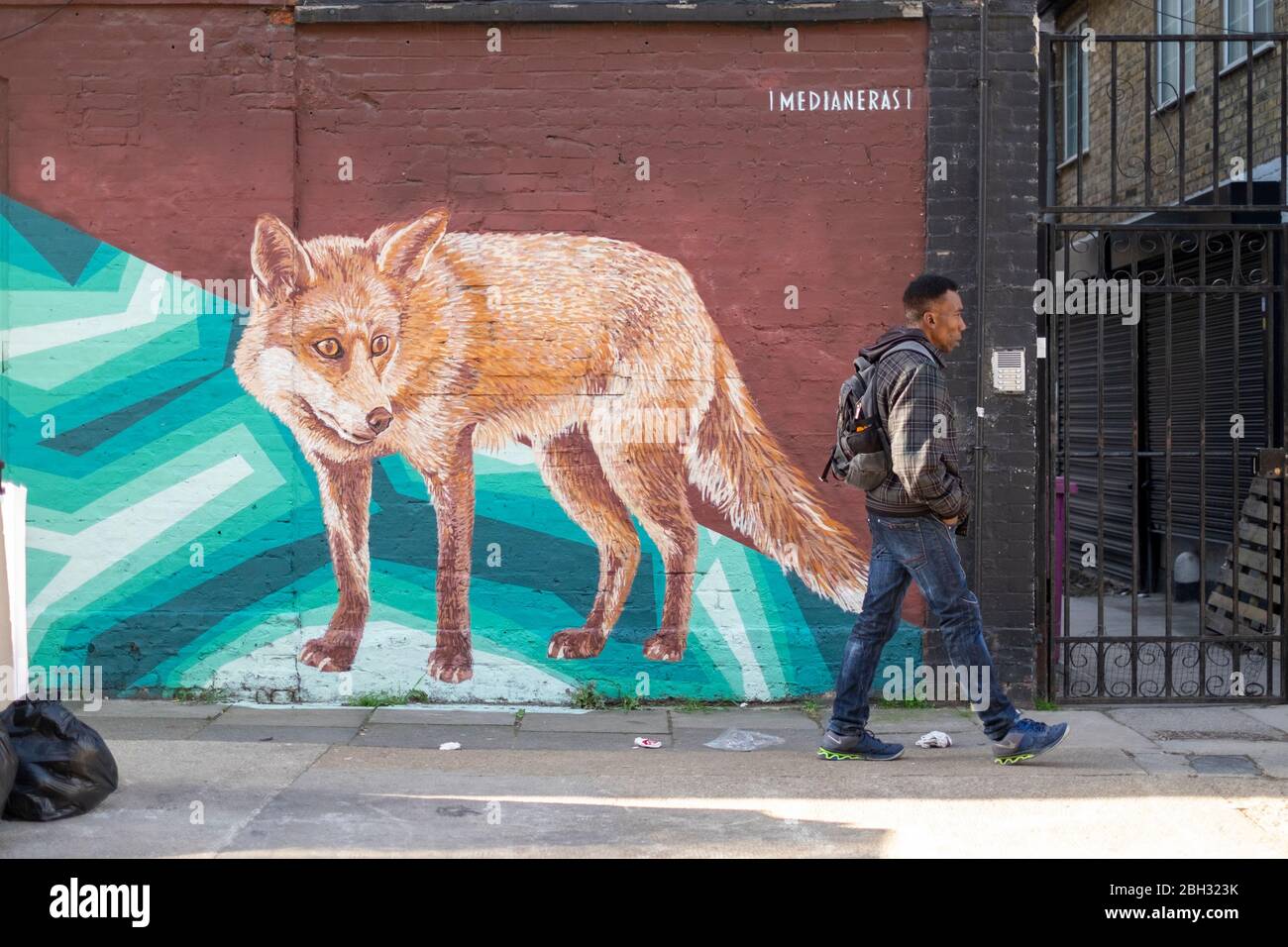 Street view of a man walking past a mural of a fox at Brick Lane, London Stock Photo