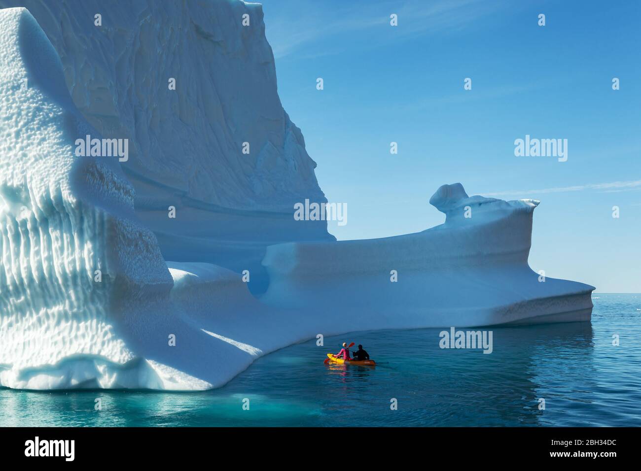 A couple kayaking around an iceberg in Greenland during summer Stock Photo
