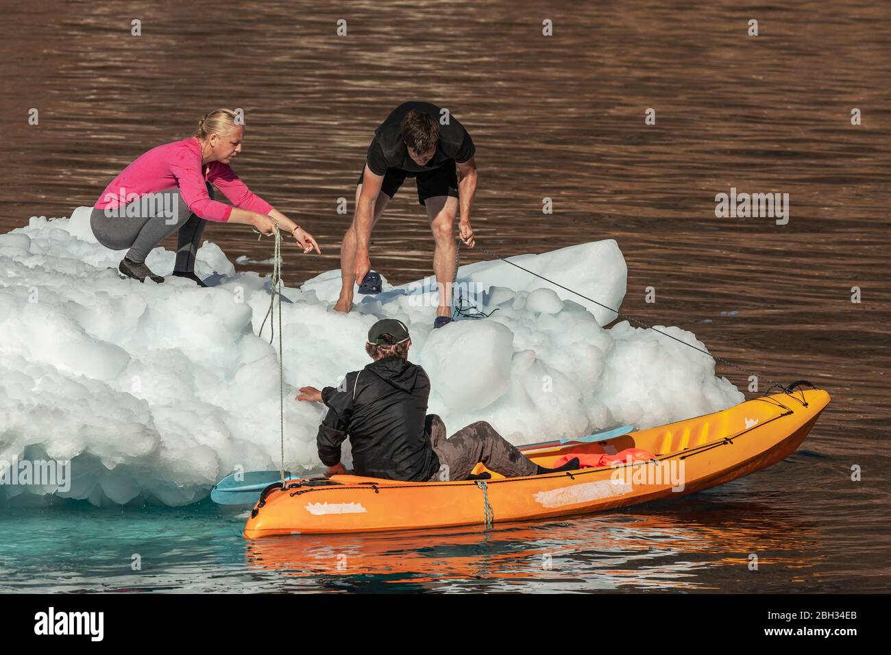 A mixed group, including a child, standing on an iceberg floating in sea, with a yellow kayak next to the iceberg Stock Photo