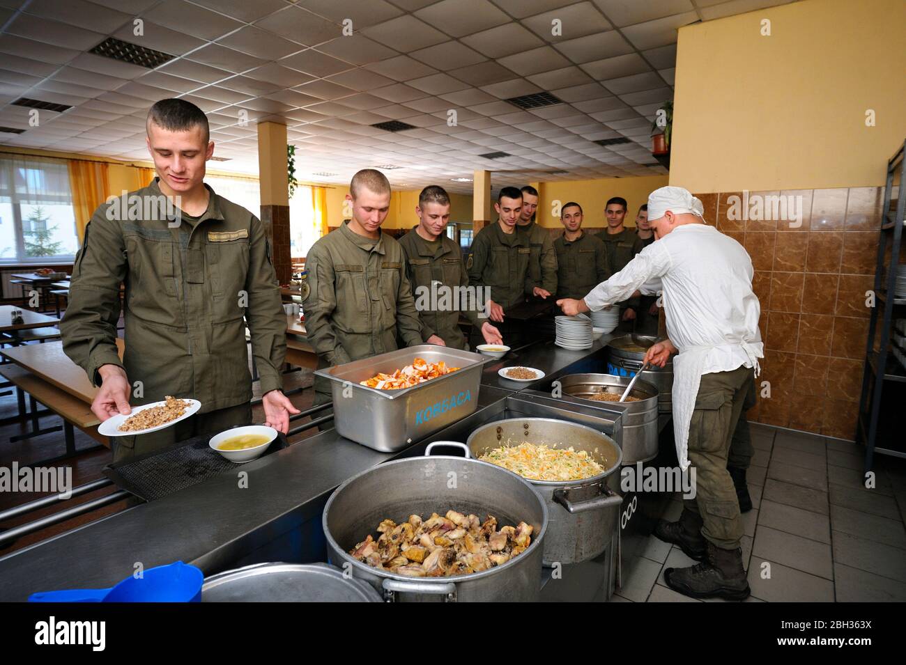 At a chow hall: soldiers stand in front of a serving bar and wait for kitchen worker preparing meal for distribution. Novo-Petrivtsi military base, Uk Stock Photo