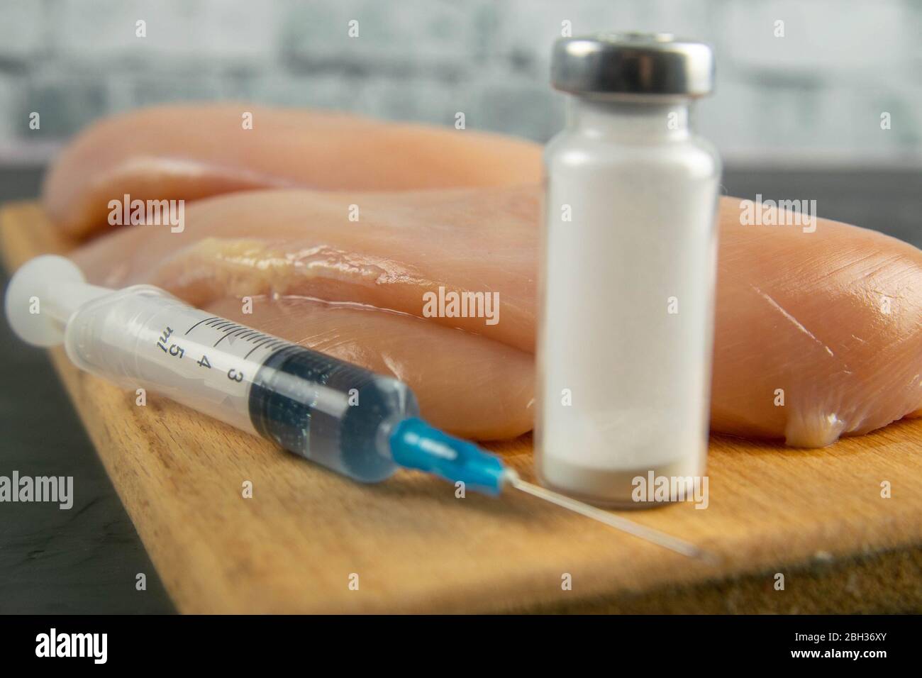 Injection syringe in raw chicken pieces, concept of injection of GMOs into the meat. Closeup