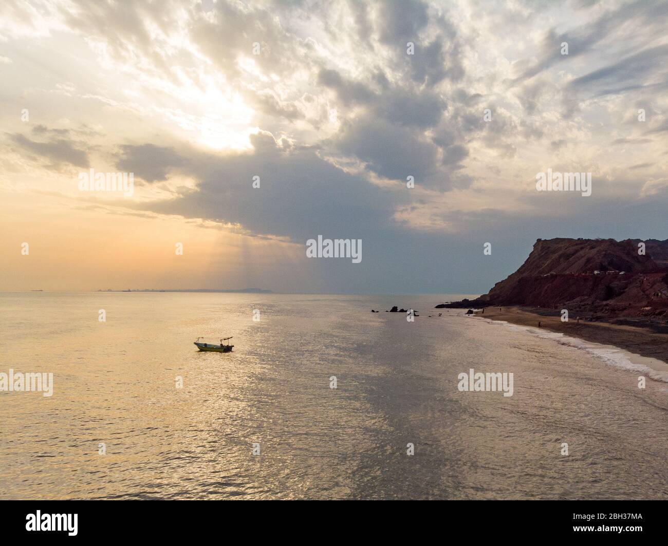 A boat is floating over the sea in front of the beautiful Silver beach named after its silver sand in the island of Hormuz in Iran at sunset time. Stock Photo