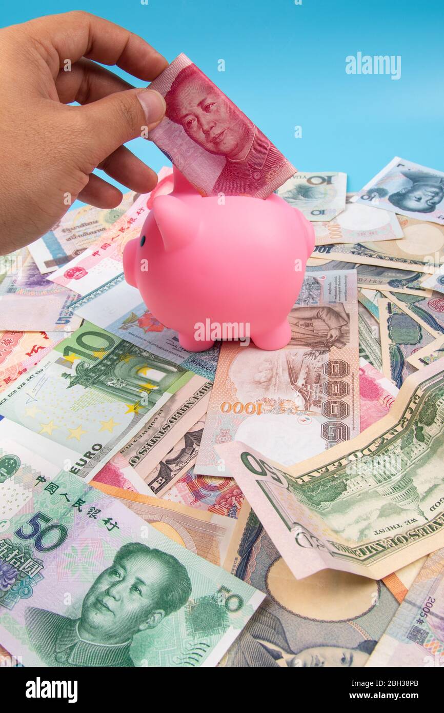 Man hand holding RMB YUAN bank note into piggy bank with World ...