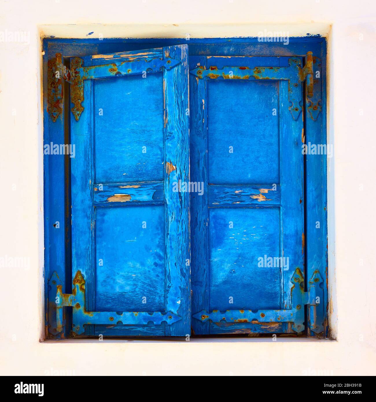 Window of greek whitewashed house with closed trditional blue shutters