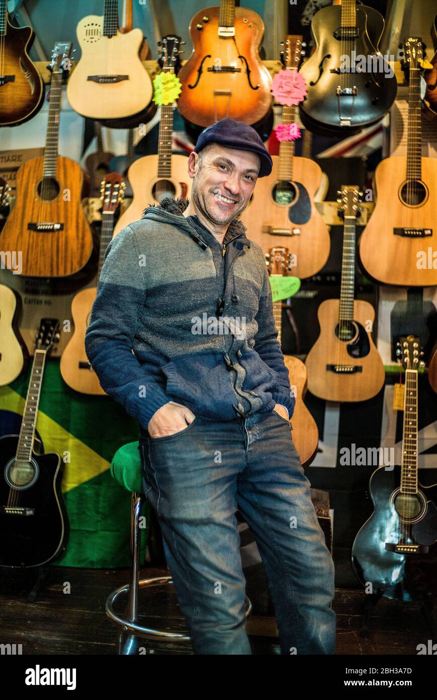Owner Deicola Neves proud guitar shop owner posing in front of instruments hanging on wall behind him Stock Photo