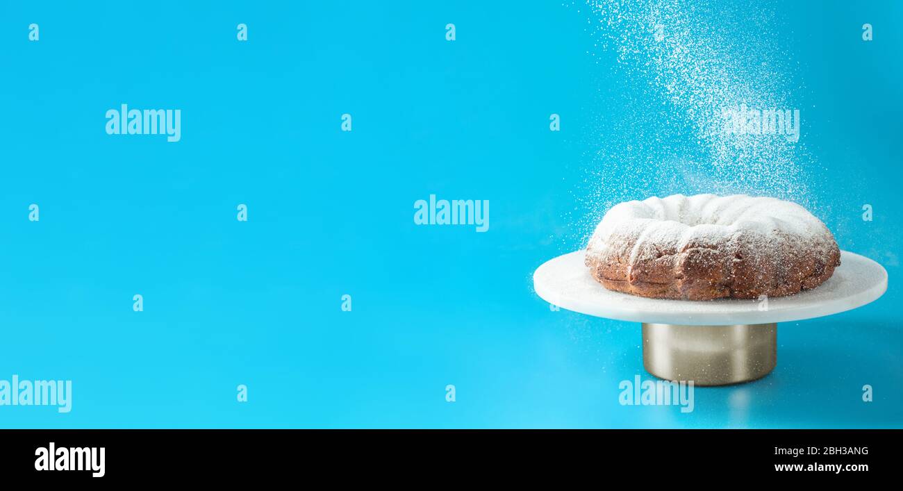 Icing sugar falling of fresh home made bundt cake. Powder sugar falls on fresh bunt cake over blue background. Copy space for text. Ideas and recipes for breakfast or dessert. Banner Stock Photo