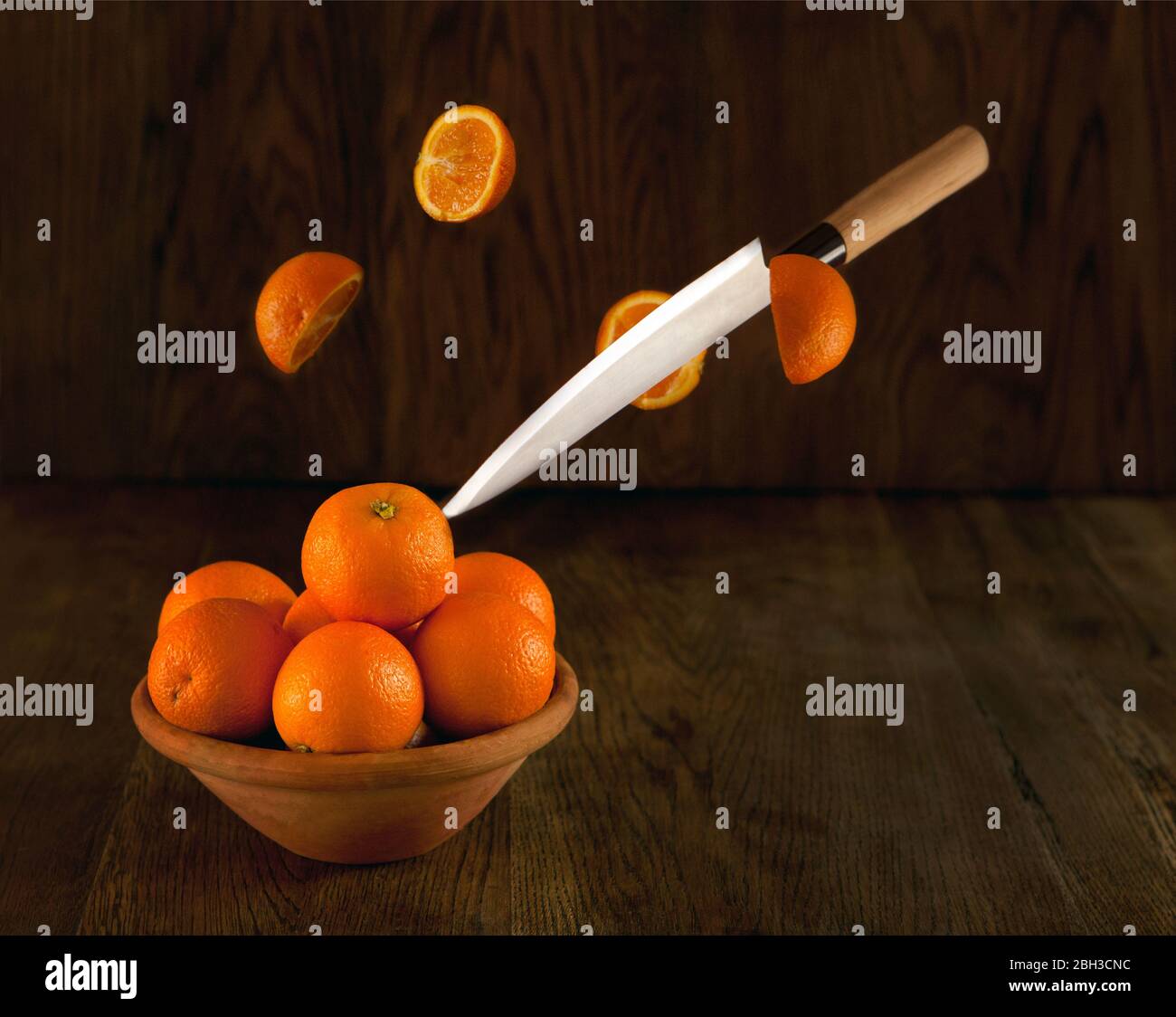 Knife cutting oranges. A lot of oranges on the bowl dark background