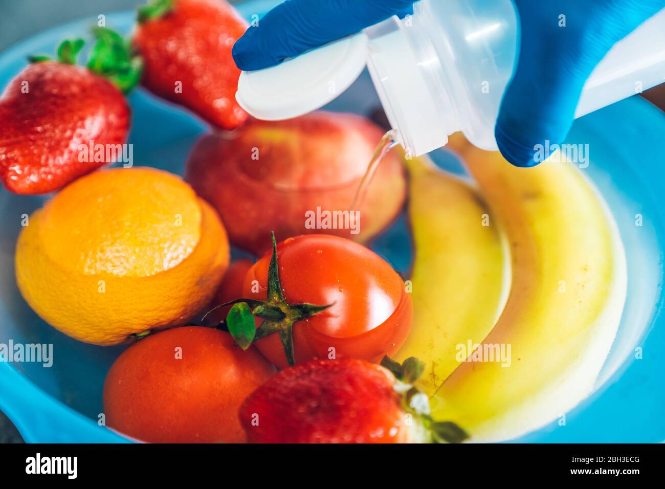 Hand with blue latex gloves pouring bleach into a plastic bowl