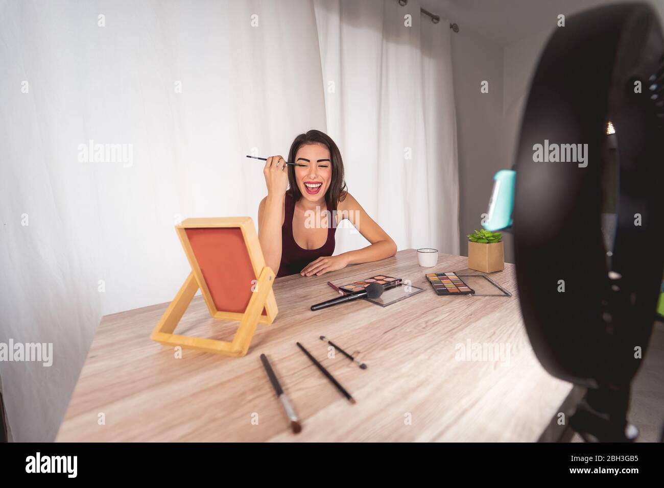 Young female vlogger doing makeup tutorial video for web channel at home - Happy influencer girl having fun filming with mobile smartphone Stock Photo