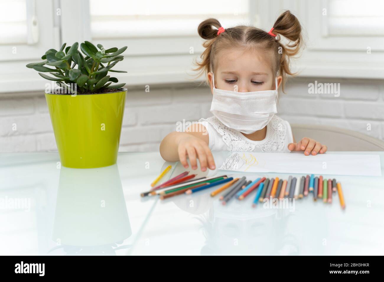 little girl in a disposable mask draws with crayons at the table. self ...