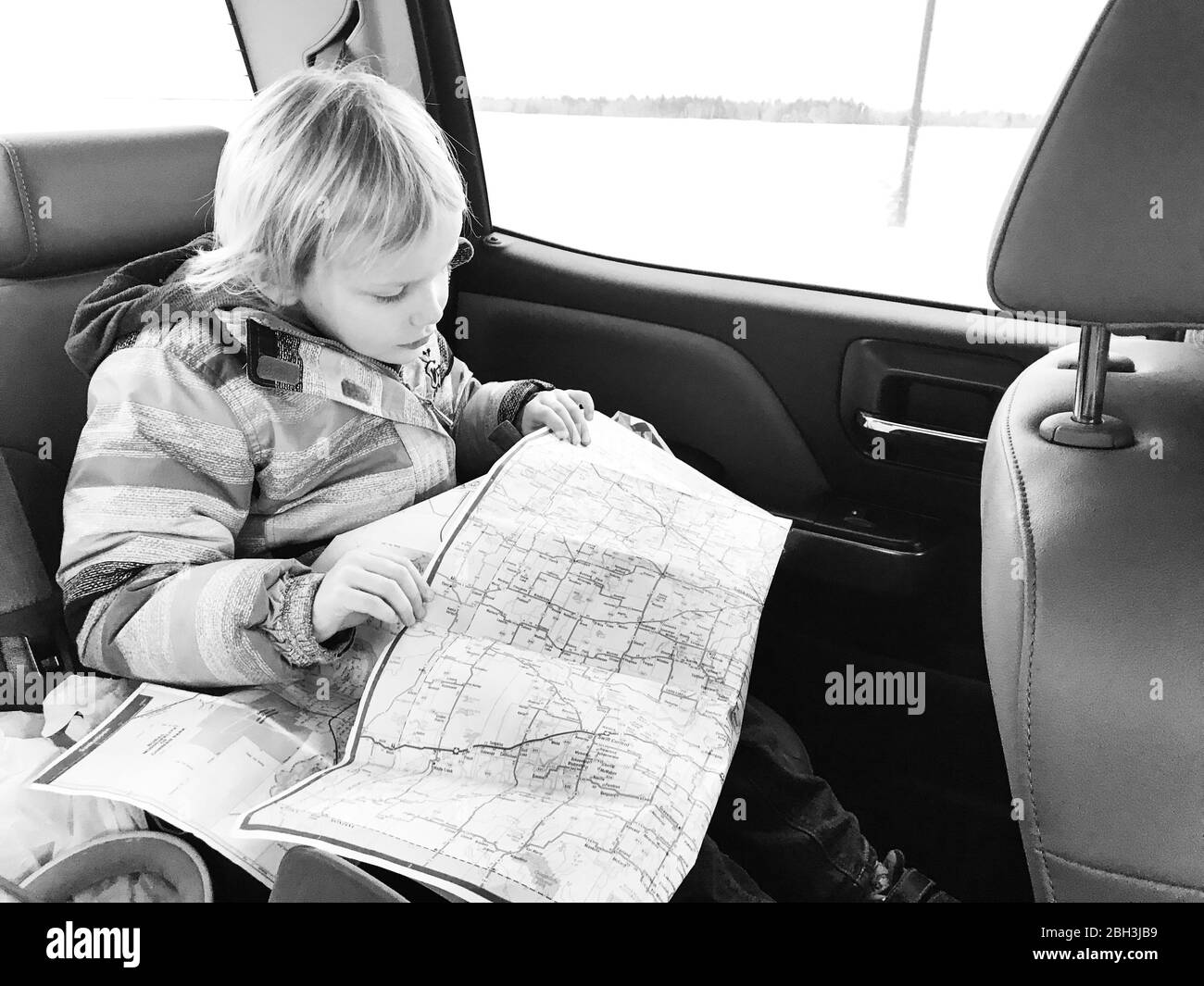 A little girl sitting in the backseat of a vehicle looking at a road