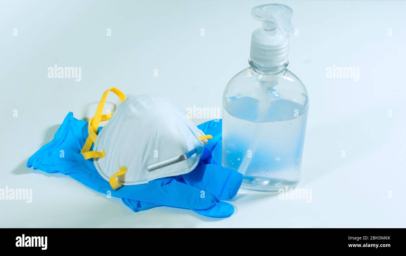 Close up view of plastic bottle with alcohol gel, white face mask and blue latex gloves on white background Stock Photo