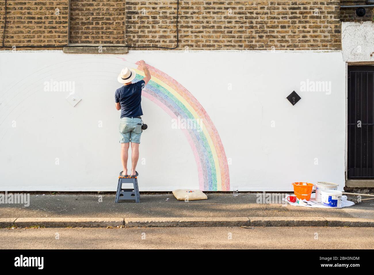 Camberwell, London, UK. 23rd April 2020. Louis Young draws a mural of a rainbow on the wall of his house to say thank you to the NHS for looking after his father. His father came out of hospital today after weeks of a pulminary but non covid-19 related illness. Credit: Tom Leighton/Alamy Live News Stock Photo