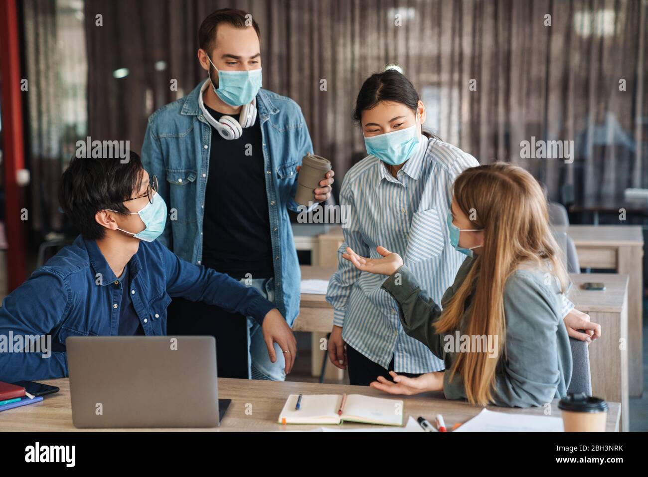 Image of multinational joyful students in protective mask talking while studying with laptop at classroom Stock Photo