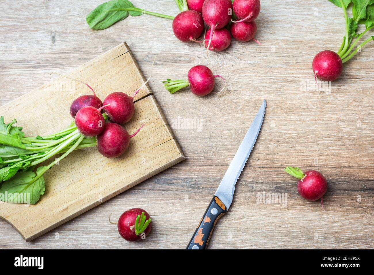 Fresh organic red radishes with green leaves on wooden background. Top