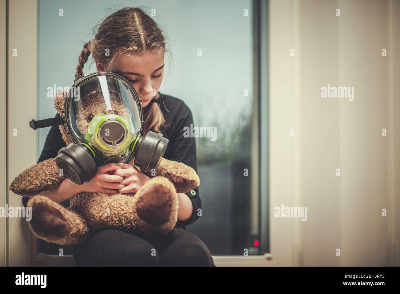 Female Child Sitting By Window Hugging Teddy Bear With Respiratory Mask On. Stock Photo