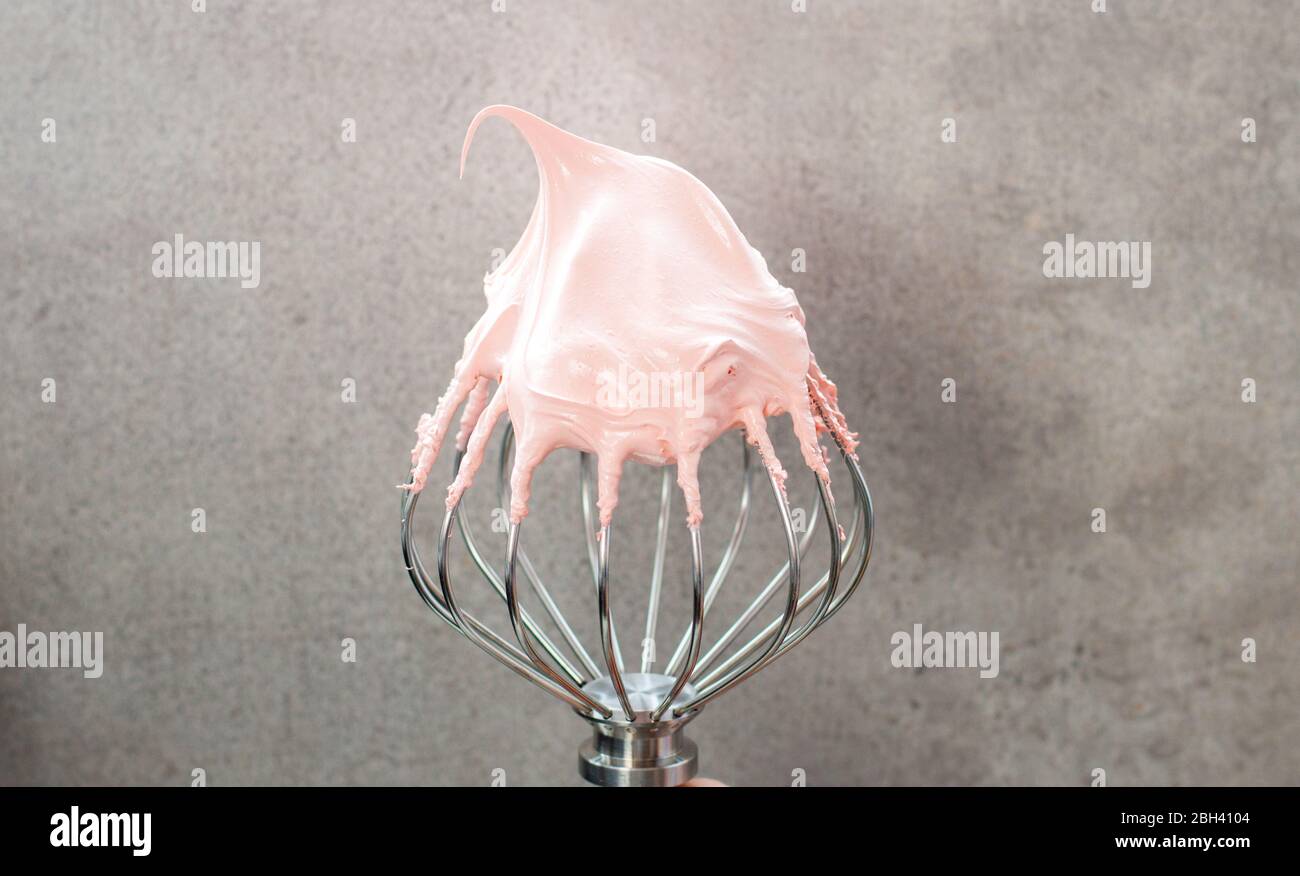 Pink whipped swiss meringue cream on top of large metal beater. Plain grey background Stock