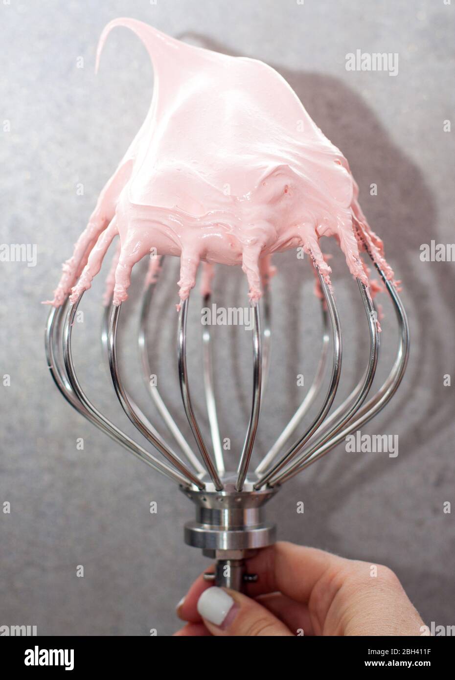 Pink whipped swiss meringue cream on top of large metal beater. Plain grey background Stock