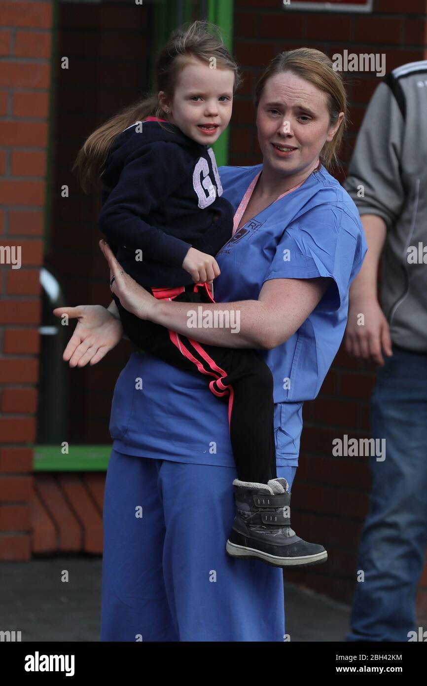 Theatre staff nurse Laura Shannon holds her daughter Eimear, 5, as they appauld pipers from the Bessbrook Crimson Arrow Pipe Band who played outside Daisy Hill Hospital in Newry, Northern Ireland, to salute local heroes during Thursday's nationwide Clap for Carers initiative to recognise and support NHS workers and carers fighting the coronavirus pandemic. Stock Photo