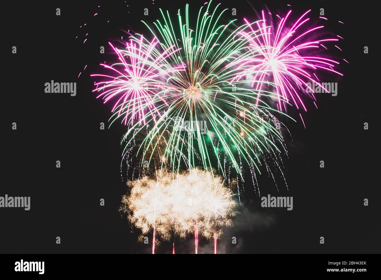 Green and purple fireworks mid explosion against a dark night sky Stock Photo