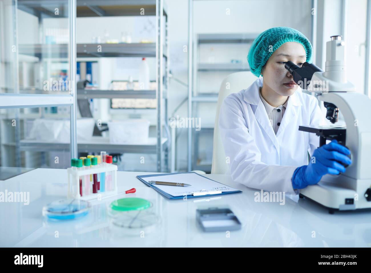 Female doctor looking through the microscope and examining the analysis ...