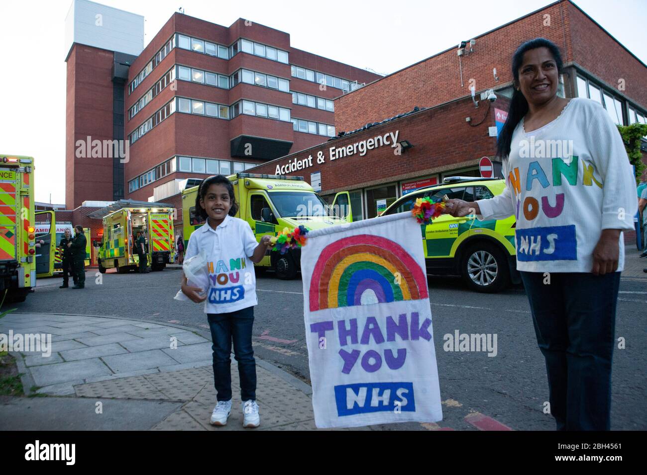 London, UK, 23 April 2020: medical and support staff gathered at the A&E ambulance bay at St George's Hospital, Tooting, to join Clap For Our Carers. This 4-year old girl, Eden, had made a rainbow banner and she and her mother wore home-made 'Thank You NHS' t-shirts. Anna Watson/Alamy Live News Stock Photo
