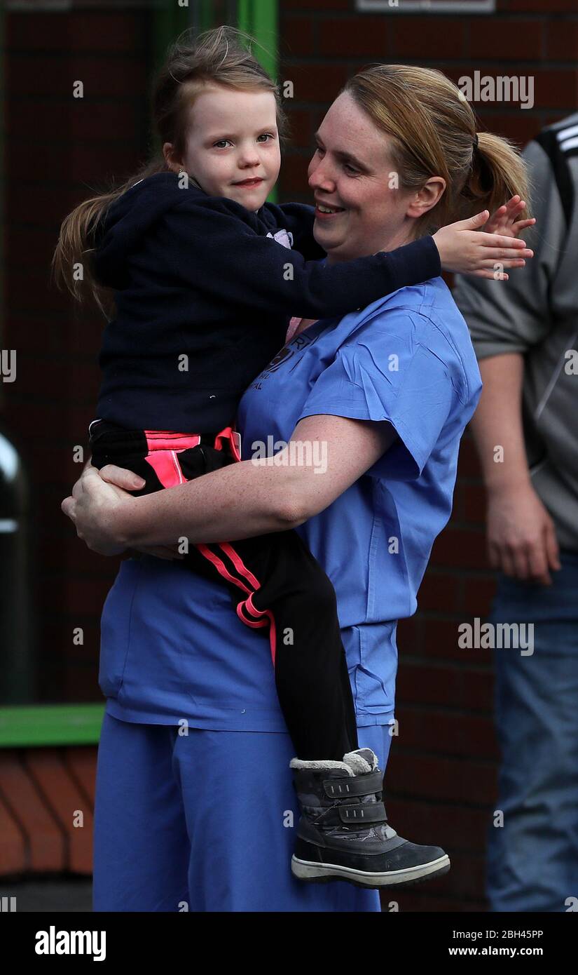 Theatre staff nurse Laura Shannon holds her daughter Eimear, 5, as they applaudd pipers from the Bessbrook Crimson Arrow Pipe Band who played outside Daisy Hill Hospital in Newry, Northern Ireland, to salute local heroes during Thursday's nationwide Clap for Carers initiative to recognise and support NHS workers and carers fighting the coronavirus pandemic. Stock Photo
