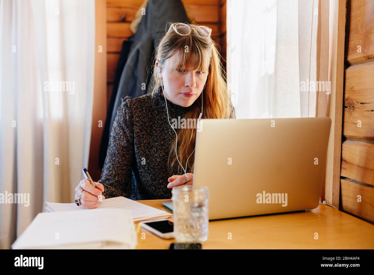 Businesswoman working on laptop computer taking notes and running her business from home during the covid-19 stay at home order.  Covid-19 pandemic Stock Photo