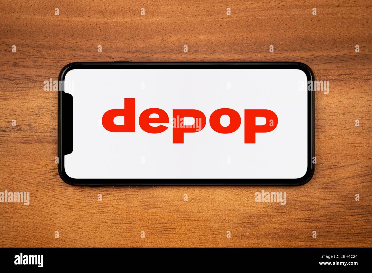 A smartphone showing the Depop logo rests on a plain wooden table (Editorial use only). Stock Photo