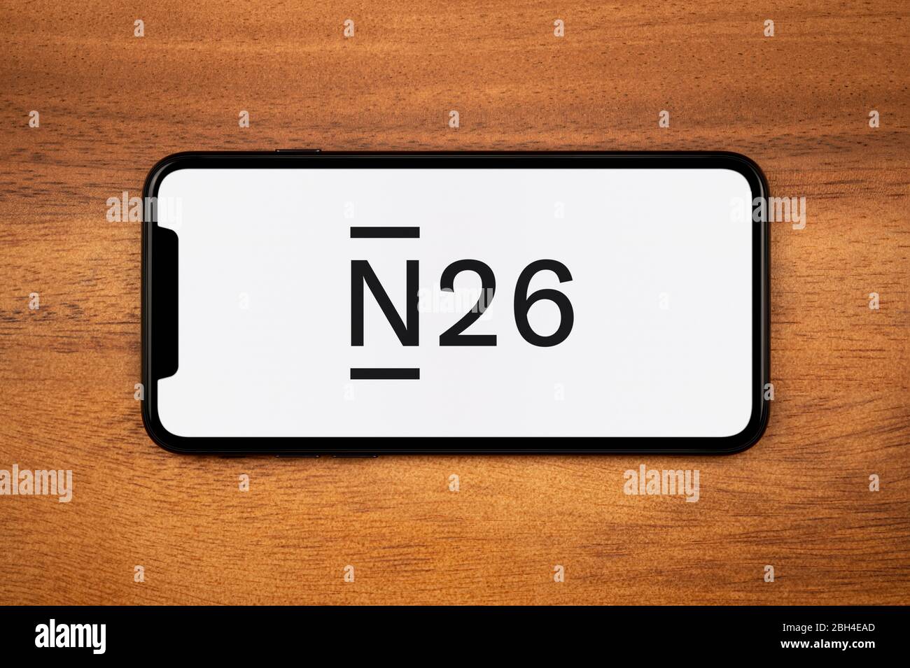 A smartphone showing the N26 logo rests on a plain wooden table (Editorial use only). Stock Photo