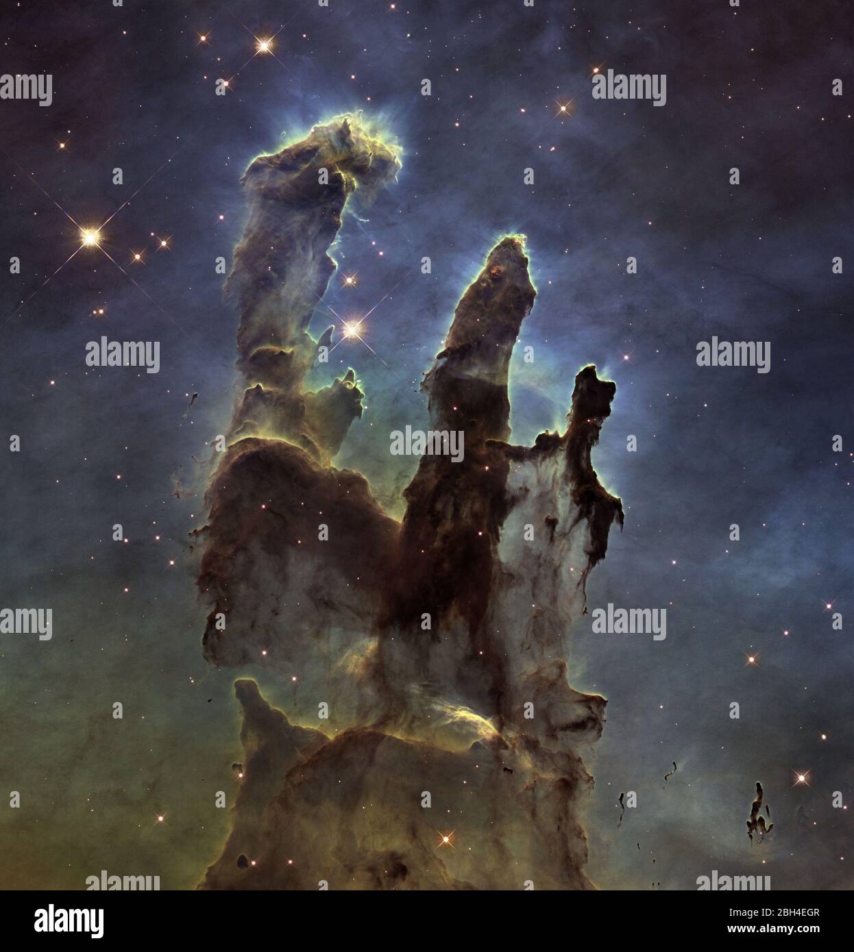 The NASA/ESA Hubble Space Telescope has revisited one of its most iconic and popular images: the Eagle Nebula's Pillars of Creation. This image shows the pillars as seen in visible light, capturing the multi-colored glow of gas clouds, wispy tendrils of dark cosmic dust, and the rust-colored elephants' trunks of the nebula's famous pillars. The dust and gas in the pillars are seared by the intense radiation from young stars and eroded by strong winds from massive nearby stars. Stock Photo