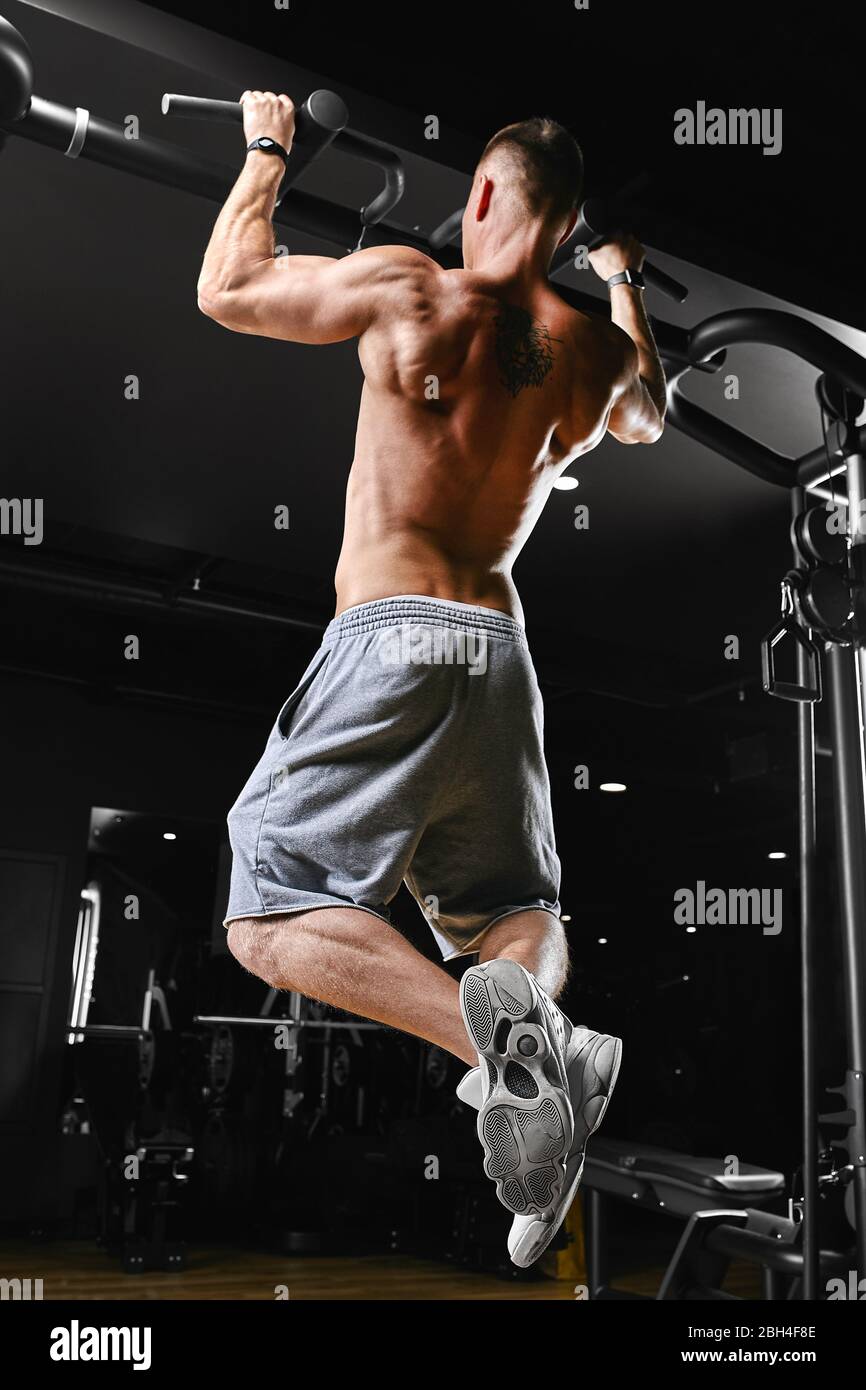 A man does pull-ups on the horizontal bar gym, a dark background, a beautiful body, Fitness motivation. Stock Photo