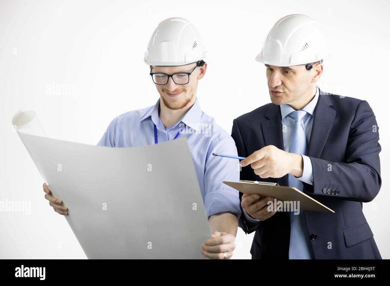 Two positive construction engineers look at drawing, making notes on clipboard Stock Photo