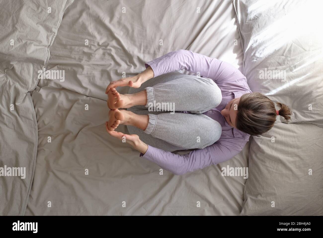 woman doing exercise for spine on bed, lying in Knees to Chest pose
