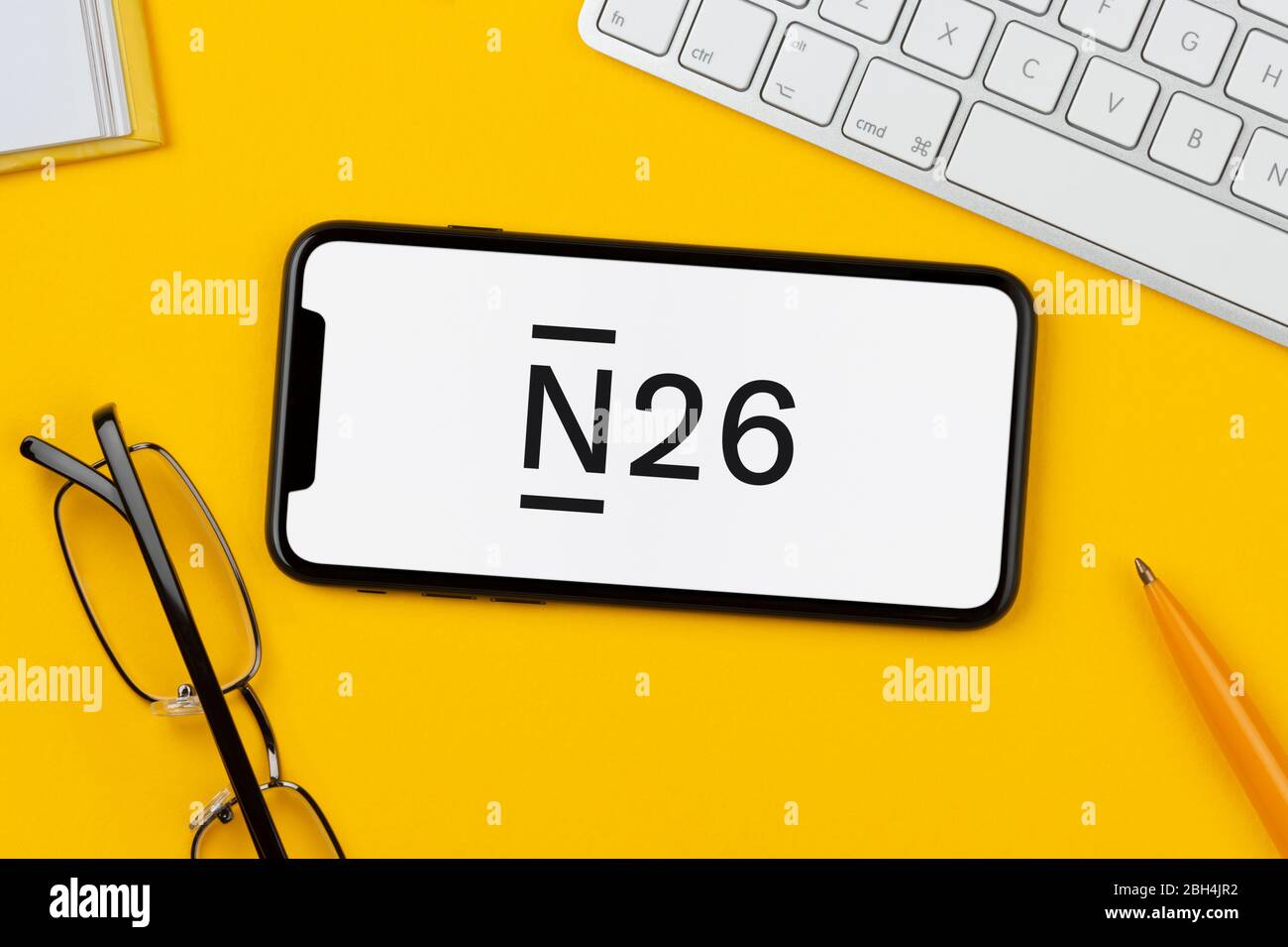 A smartphone showing the N26 logo rests on a yellow background along with a keyboard, glasses, pen and book (Editorial use only). Stock Photo