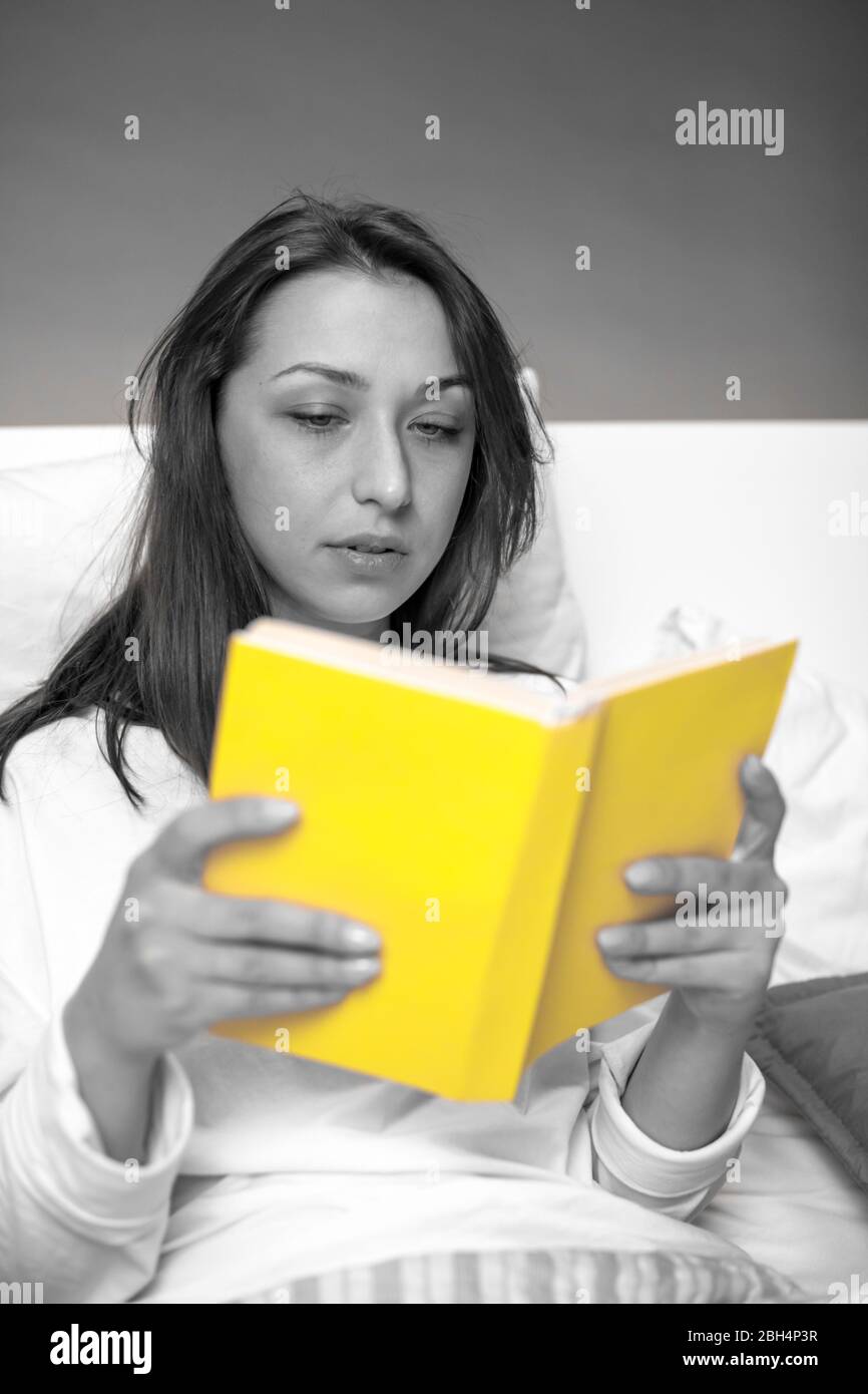 cute darkhaired girl in pajamas reading book with yellow cover sitting in bed Stock Photo Alamy