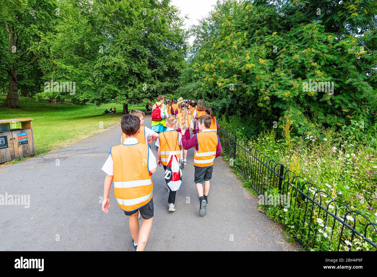 London, UK - June 21, 2018: St James Park green trees in summer with many crowd of people school children walking on sidewalk road on field trip in ve Stock Photo